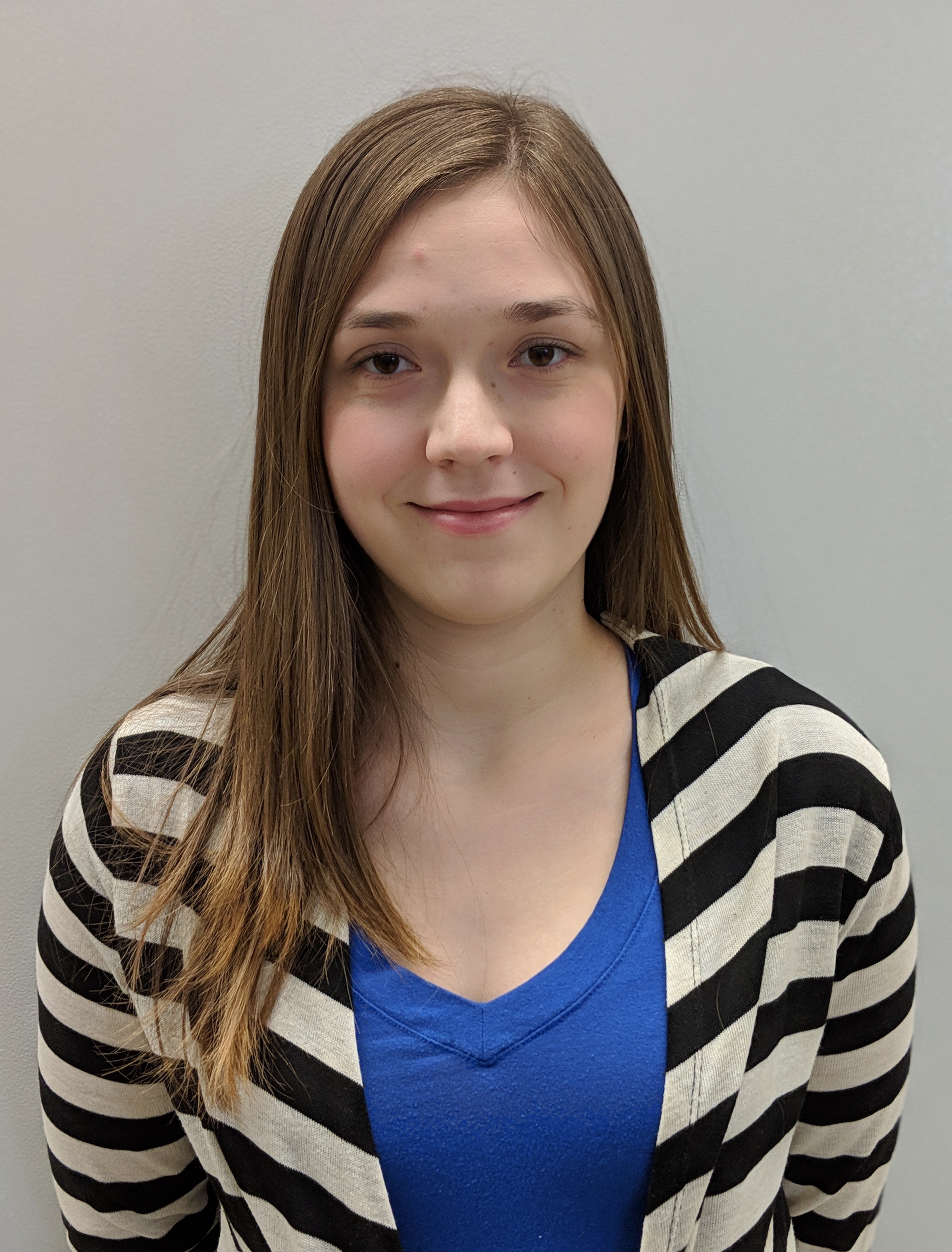 A white woman with long, light brown hair, wearing a striped cardigan over a blue shirt smiling in a headshot in front of a neutral background..